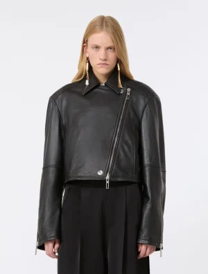 Model wearing a black leather biker jacket with an asymmetrical zipper and silver hardware, paired with black trousers and statement earrings.