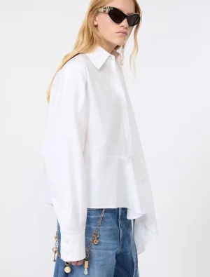Model in an oversized white shirt, blue jeans, and black sunglasses, with a gold chain accessory at the hip.
