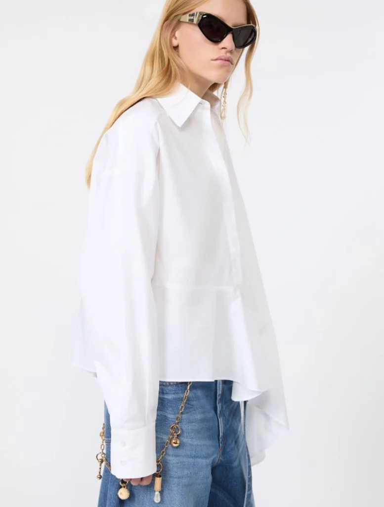 Model in an oversized white shirt, blue jeans, and black sunglasses, with a gold chain accessory at the hip.