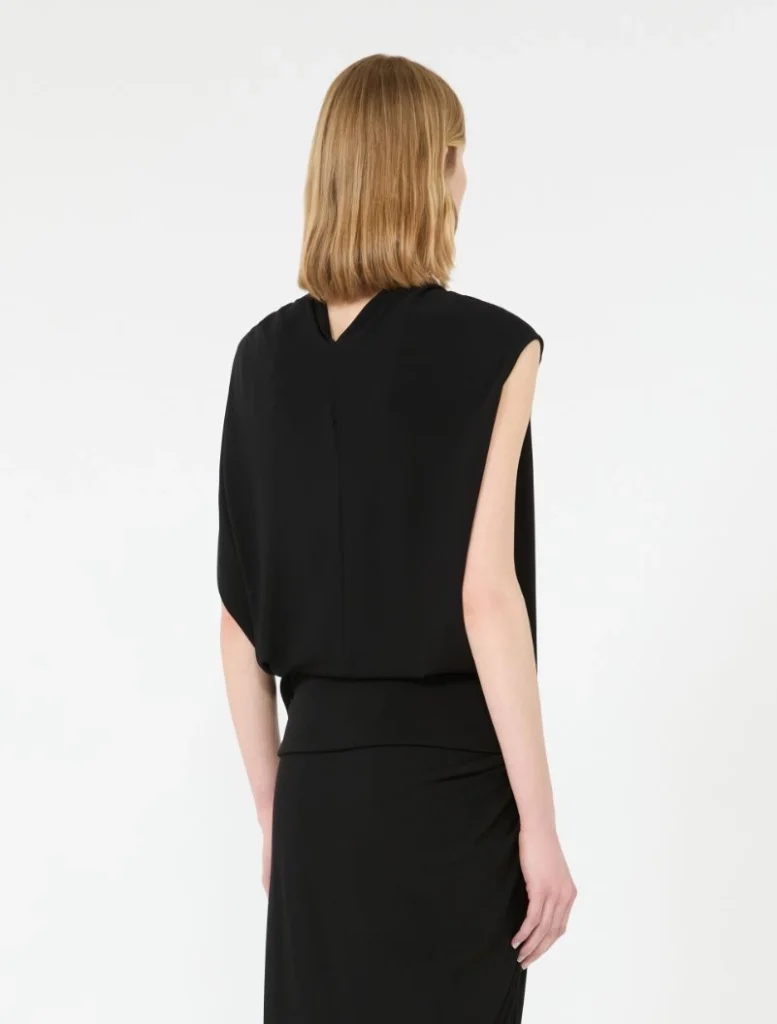 Back view of a woman wearing a black sleeveless top and long black skirt against a white background.
