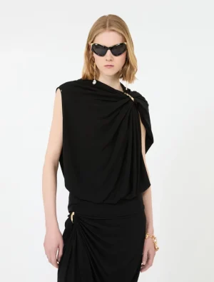 Model in a black draped one-shoulder top with a matching ruched skirt and gold jewelry, wearing large sunglasses.