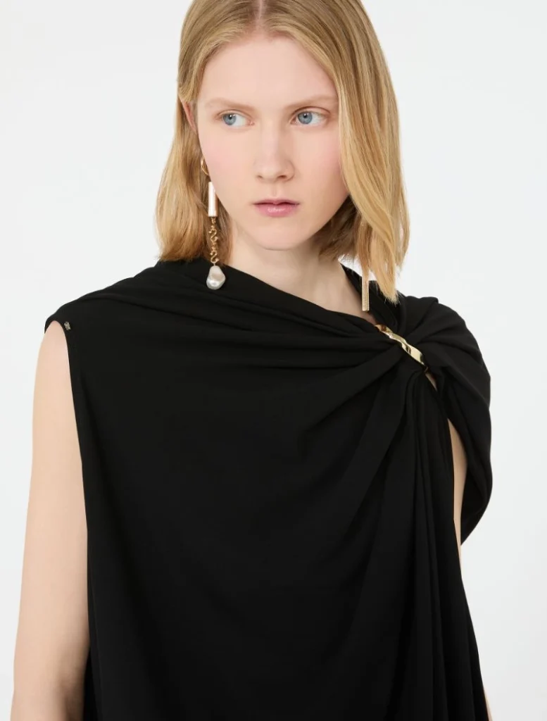 Model wearing a black draped sleeveless top with a gold chain earring and pearl pendant on the left ear.