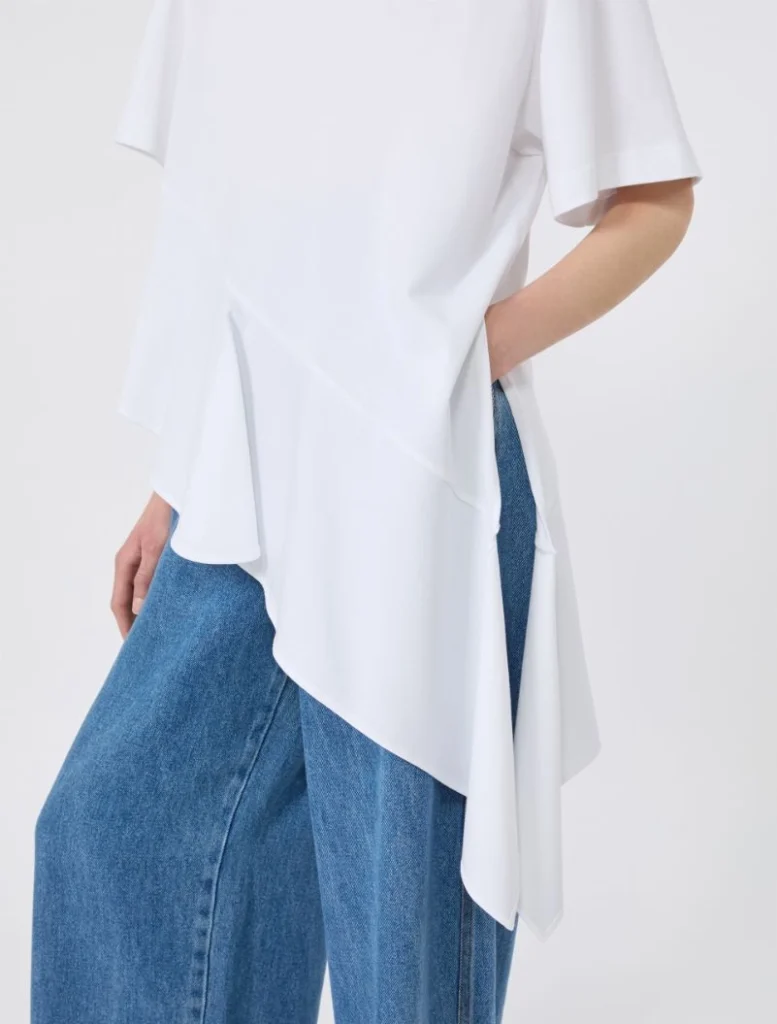 Side view of a person wearing a white asymmetrical draped top over blue jeans.