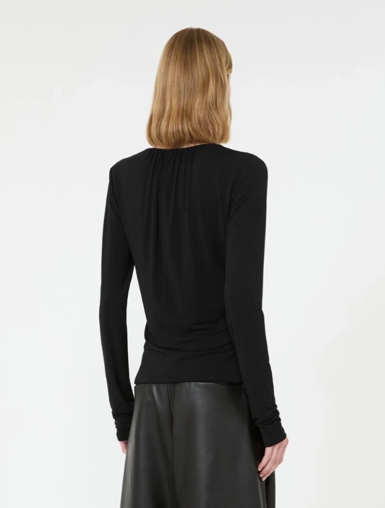 Back view of a person wearing a black long-sleeve top tucked into a black faux leather skirt, blonde hair.