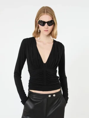 Model wearing a black ruched V-neck top with black leather pants, accessorized with oversized sunglasses and dangling earrings.