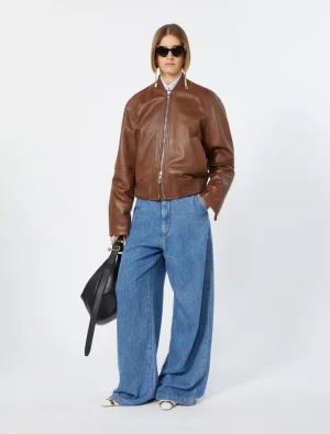 Model wearing a brown leather bomber jacket with wide-leg blue jeans, white shirt, black sunglasses, and a black handbag.