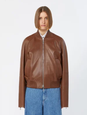 Model wearing a brown leather bomber jacket with a front zipper, ribbed collar, cuffs, and hem, paired with blue jeans (front view).