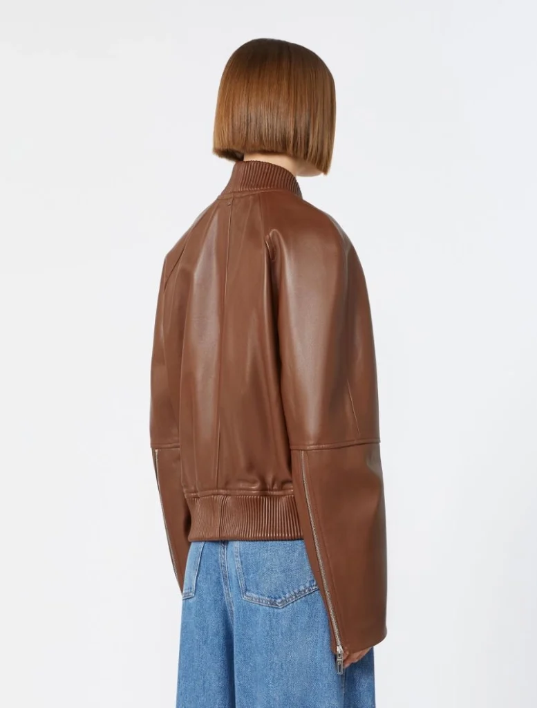 Back view of a person wearing a brown leather bomber jacket and blue jeans, with a short straight bob haircut.