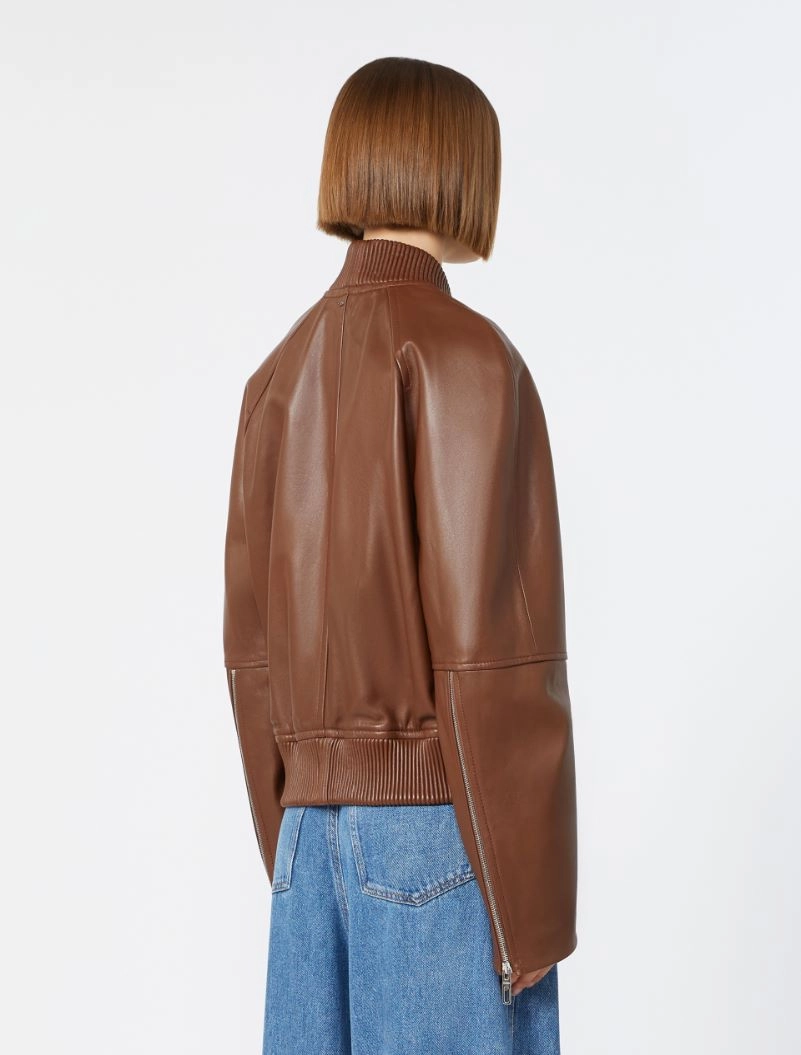 IMG_3079 - New Trend Back view of a person wearing a brown leather bomber jacket and blue jeans, with a short straight bob haircut.