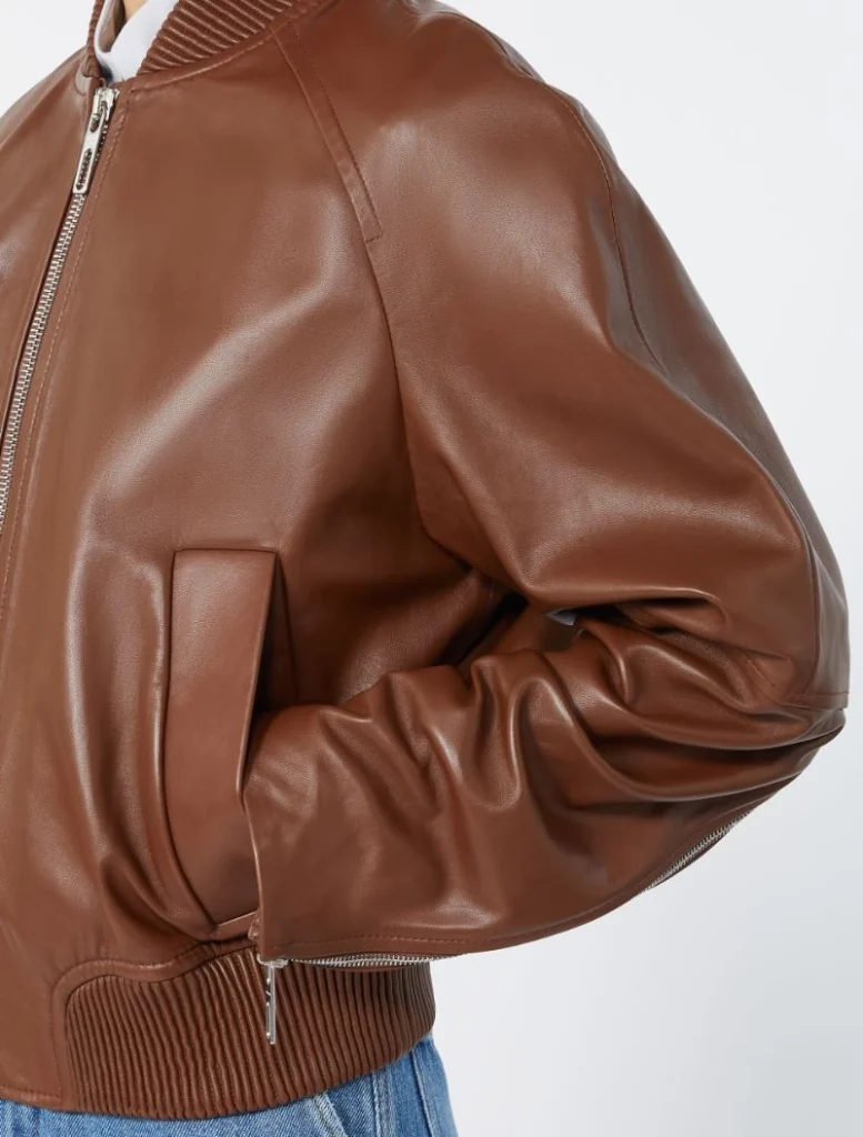Close-up of a brown leather bomber jacket sleeve with a zip, pocket, and ribbed hem detail.