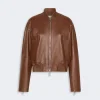 Brown leather bomber jacket with front zipper and ribbed cuffs on a light gray background.