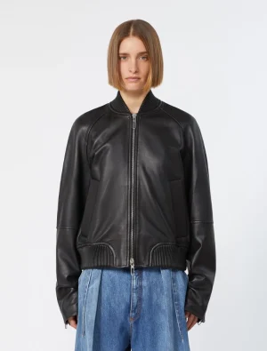 Woman wearing a black leather bomber jacket with a front zipper and ribbed cuffs, paired with blue jeans in a studio setting.