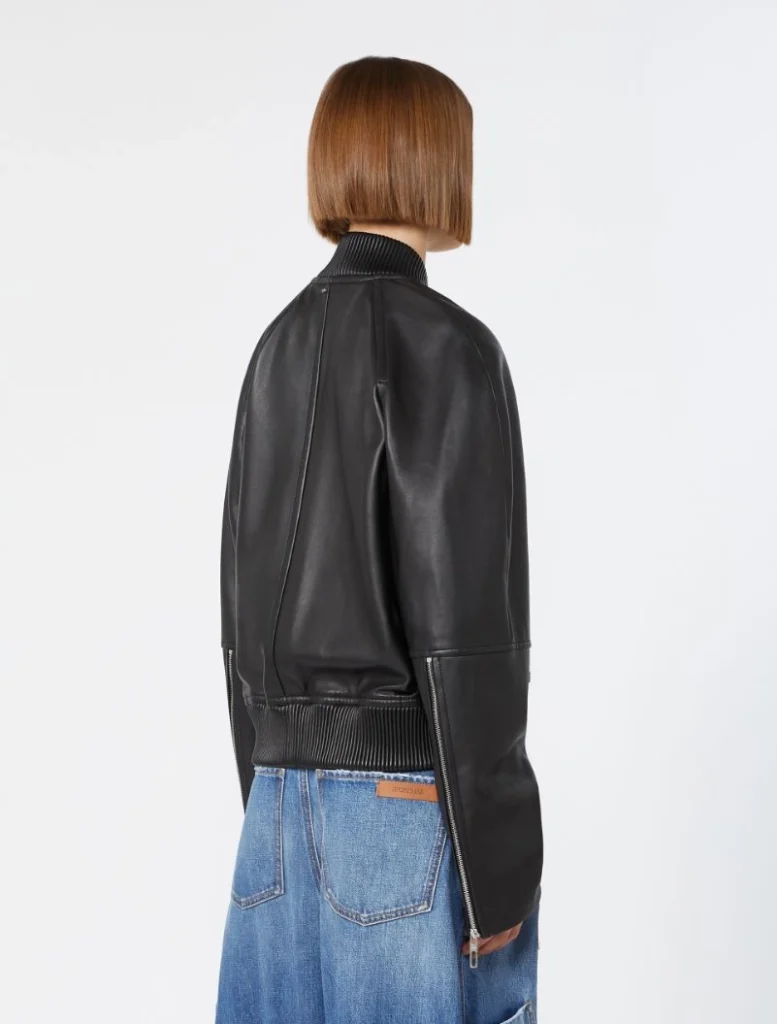 Back view of a person wearing a black leather bomber jacket with ribbed collar and waistband, paired with blue jeans.