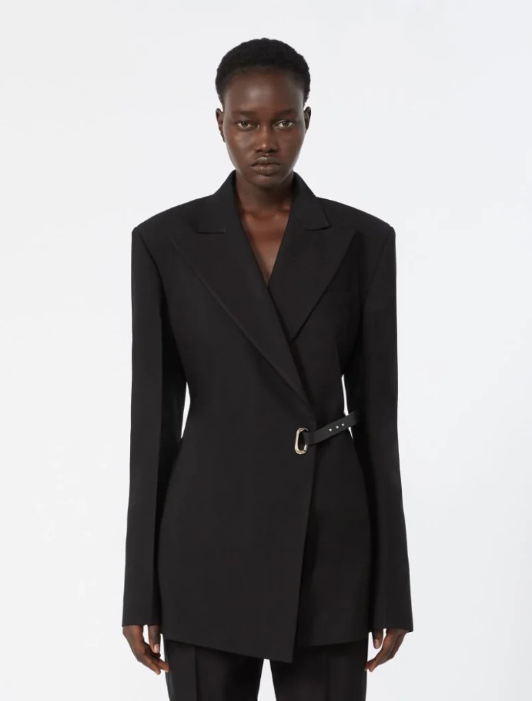 Model wearing a black structured blazer with a waist belt and asymmetric front wrap.