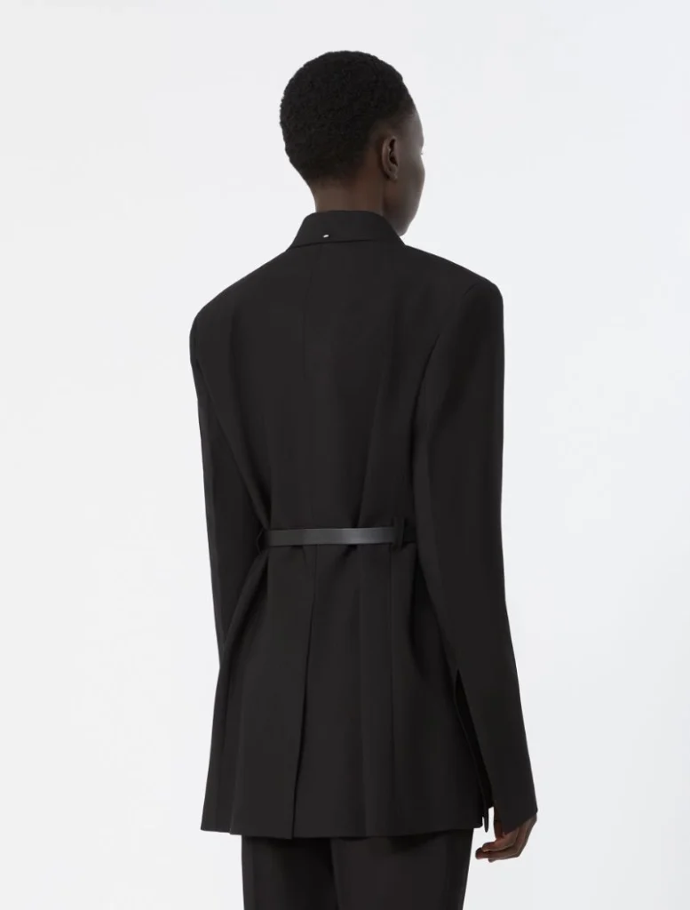 Back view of a person wearing a black tailored blazer with a belt, standing against a light background.