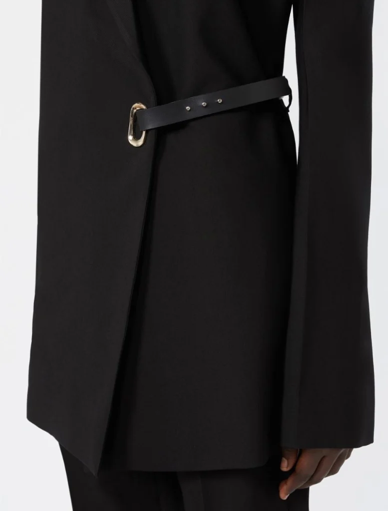 Close-up of a black coat's waist with a slim black belt and a gold buckle cinching the garment.