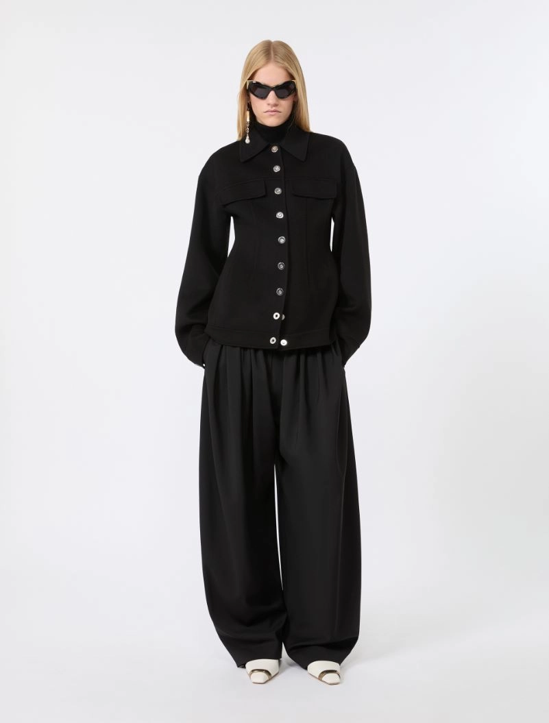 IMG_3095 - New Trend Full-body shot of a woman in an all-black outfit: button-front jacket with large pockets and wide-leg trousers, white sandals, and sunglasses.