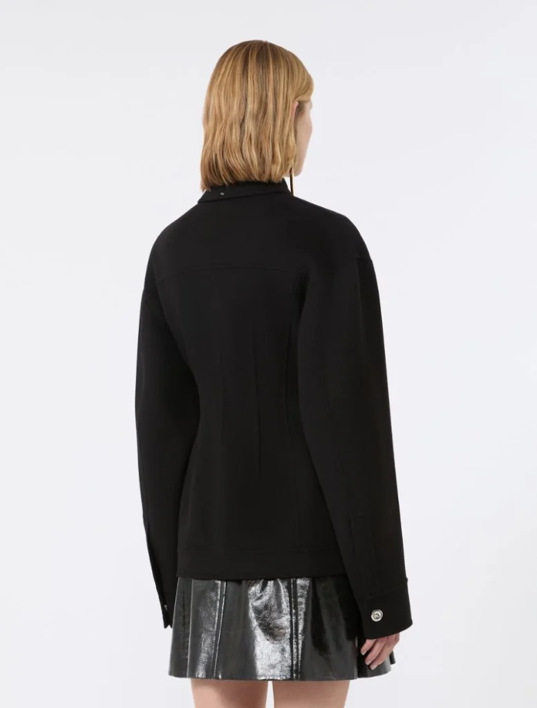 Back view of a person wearing a black tailored jacket and a metallic silver mini skirt, with short blonde hair visible from behind.