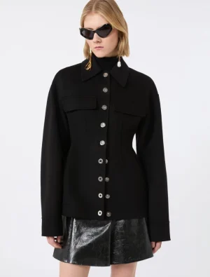 Model wearing a black button-front jacket with large chest pockets, silver buttons, and a shiny black mini skirt, plus sunglasses and earrings.