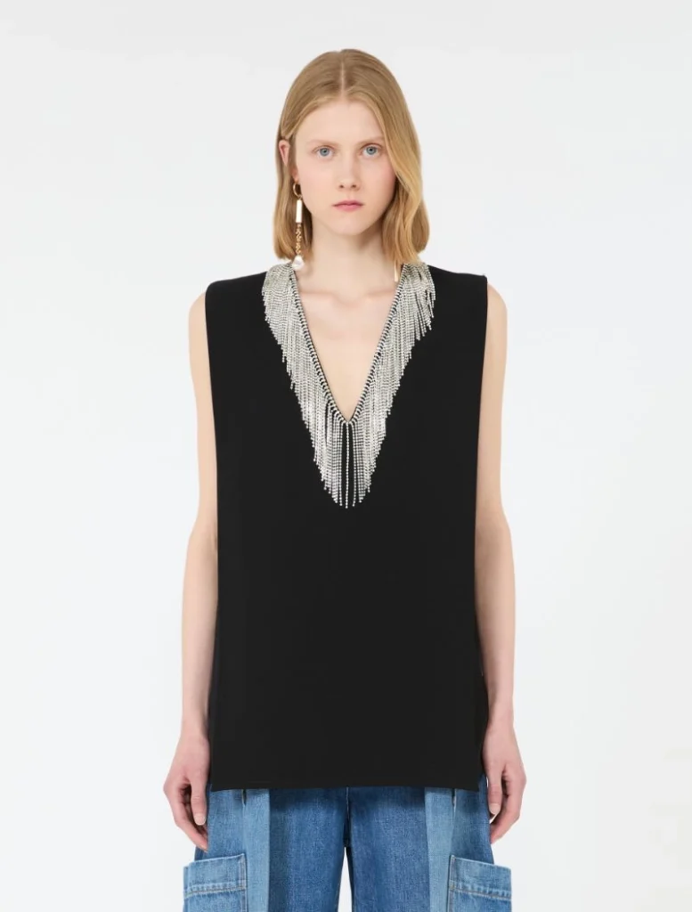 Model wearing a sleeveless black top with a silver beaded V-shaped neckline detail, paired with blue denim cargo jeans in a studio setting.