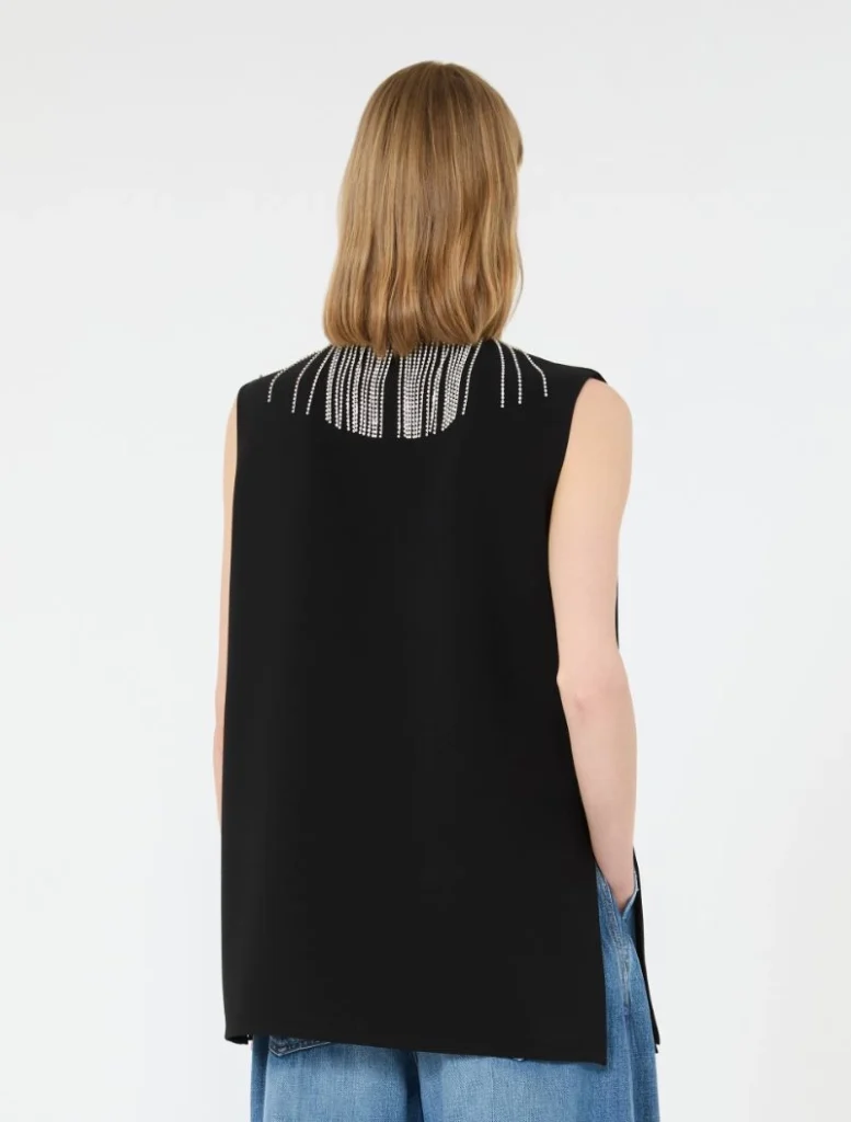 Back view of a person in a black sleeveless top with silver beaded fringe at the neckline, paired with blue jeans.