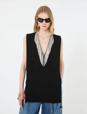 Model wearing a black sleeveless top with a silver beaded V-neck necklace and blue jeans, sunglasses on a white background.