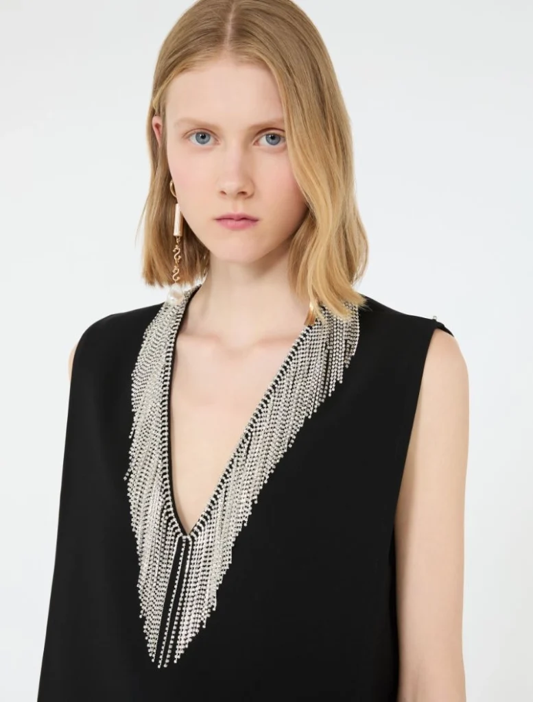 Model wearing a black sleeveless top with a long silver beaded fringe necklace.