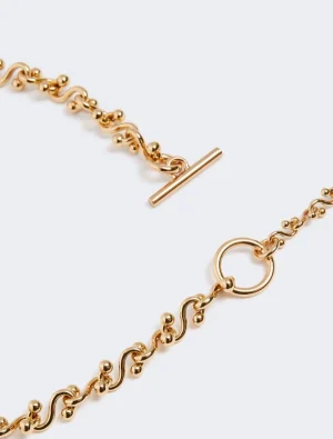 Gold-tone chain bracelet with a circular ring and T-bar toggle clasp, close-up view.
