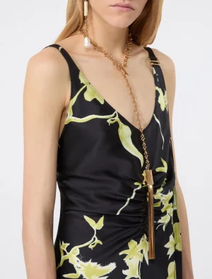 Close-up of a model wearing a black satin dress with a yellow-green floral print and a long gold tassel necklace at the V-neckline