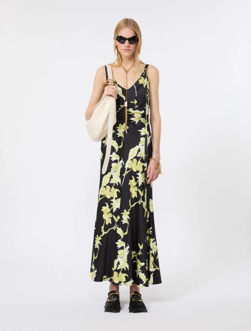 IMG_3111 - New Trend Woman in a black floral maxi dress with pale yellow-green leaves, carrying a cream tote bag and wearing sunglasses.