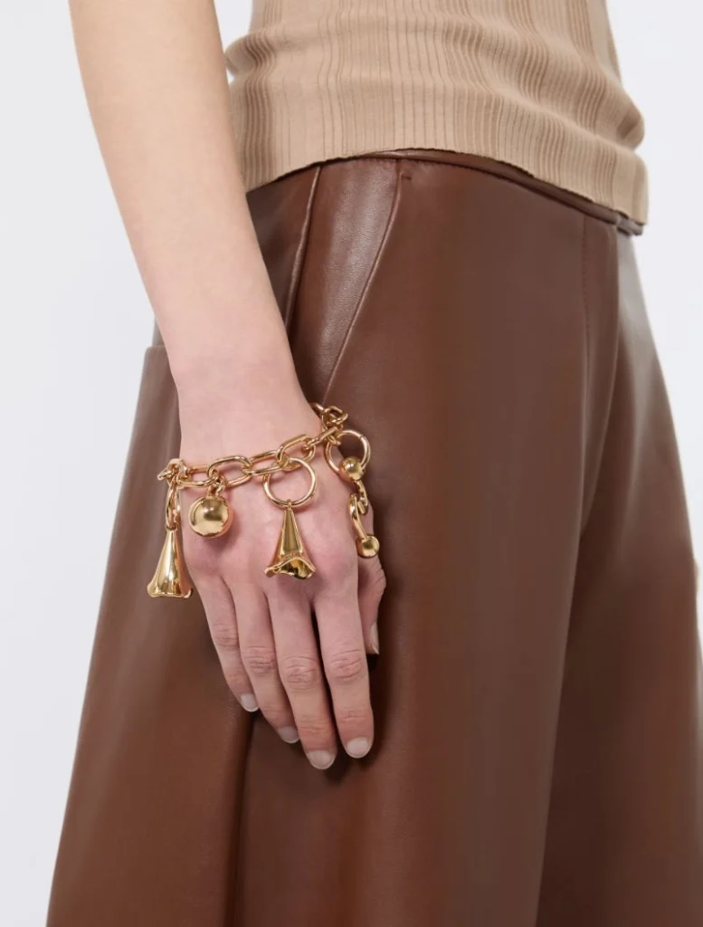 Gold charm bracelet with dangling charms on a wrist over a brown leather skirt and beige top.