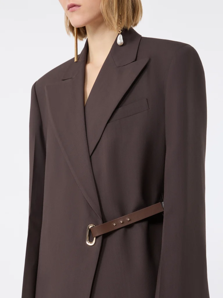 Close-up of a brown blazer with a leather belt and gold buckle, worn by a person with a pearl drop earring visible on the left.
