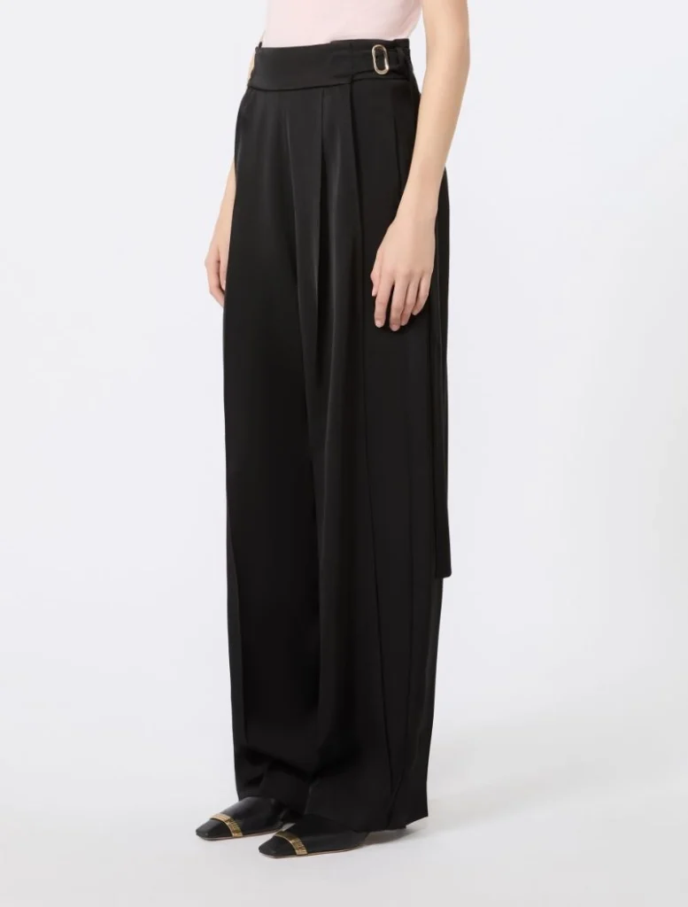 Pair of black, high-waisted wide-leg trousers with a belt detail, worn by a model in a light pink top and black loafers with gold accents.