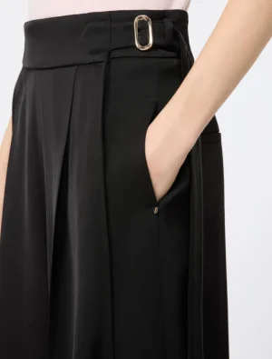 Close-up of a person wearing black wide-leg trousers with a belt buckle and hand in the side pocket.