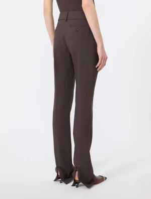 Back view of a person wearing dark brown tailored trousers with back pockets and a slight flare over pointed heels.