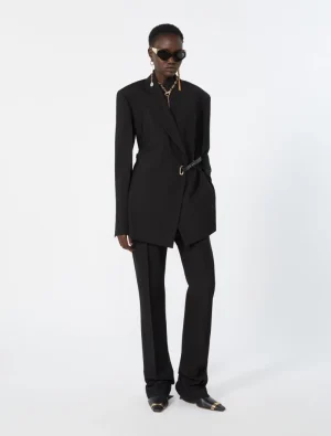 Person wearing a tailored black blazer with a belt over black wide-leg pants, accessorized with gold jewelry and dark sunglasses.