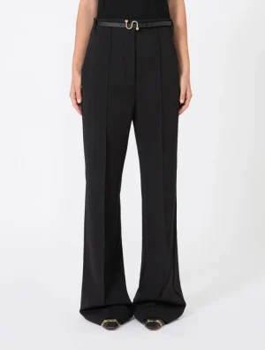Model wearing black high-waisted wide-leg trousers with a slim belt and gold buckle, paired with a black top and black shoes with gold accents.