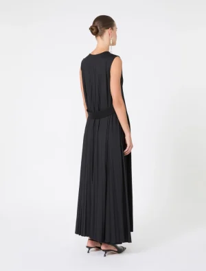 Back view of a woman in a black sleeveless maxi dress with a wide belt, her hair in a bun, wearing dangling earrings and black heeled sandals