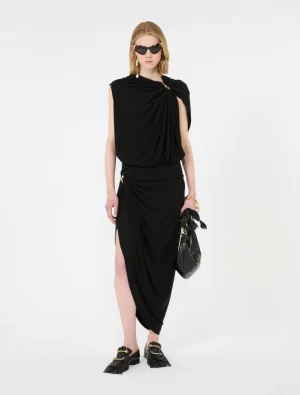 Model wearing a black draped wrap dress with a high side slit, gold jewelry, sunglasses, and black tassel loafers with gold hardware.