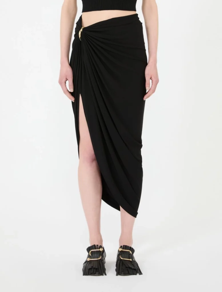 Full-length view of a black draped midi skirt with a thigh-high slit, paired with black fringe loafers.