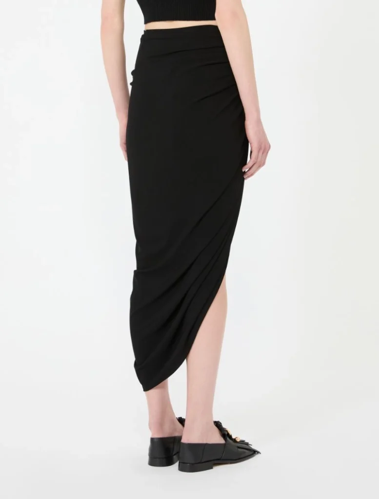 Back view of a person wearing a black draped wrap midi skirt with black flats, cropped top visible at the waist.
