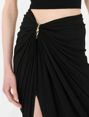 Close-up of a black draped skirt with a gold-toned clasp at the waist and a side slit visible