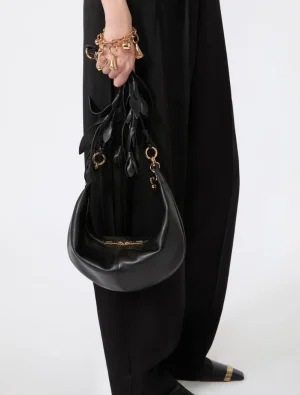 Person in black clothing holds a black leather hobo bag with gold hardware and decorative gold charms in the hand.