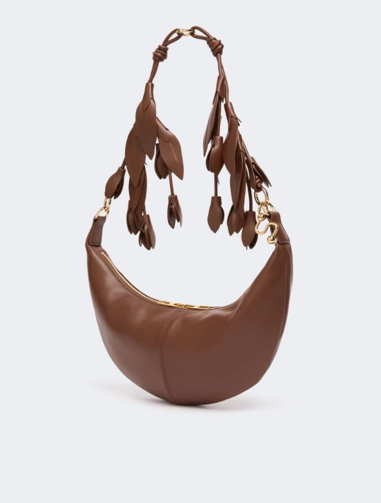Brown leather crescent handbag with fringe leaf details and gold hardware on a pale background