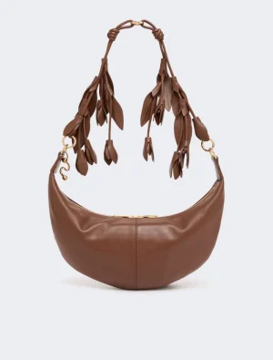 Brown leather crescent handbag with tasseled braided handles and gold hardware on a light background.