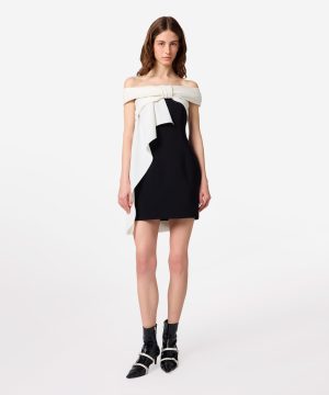 Model in a black off-shoulder mini dress with a white draped scarf tied at the bust and left to hang gracefully across the front.