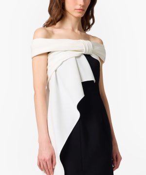 Off-shoulder black-and-white color-block dress with white draped fold across the chest and side knot detail on a model's torso.