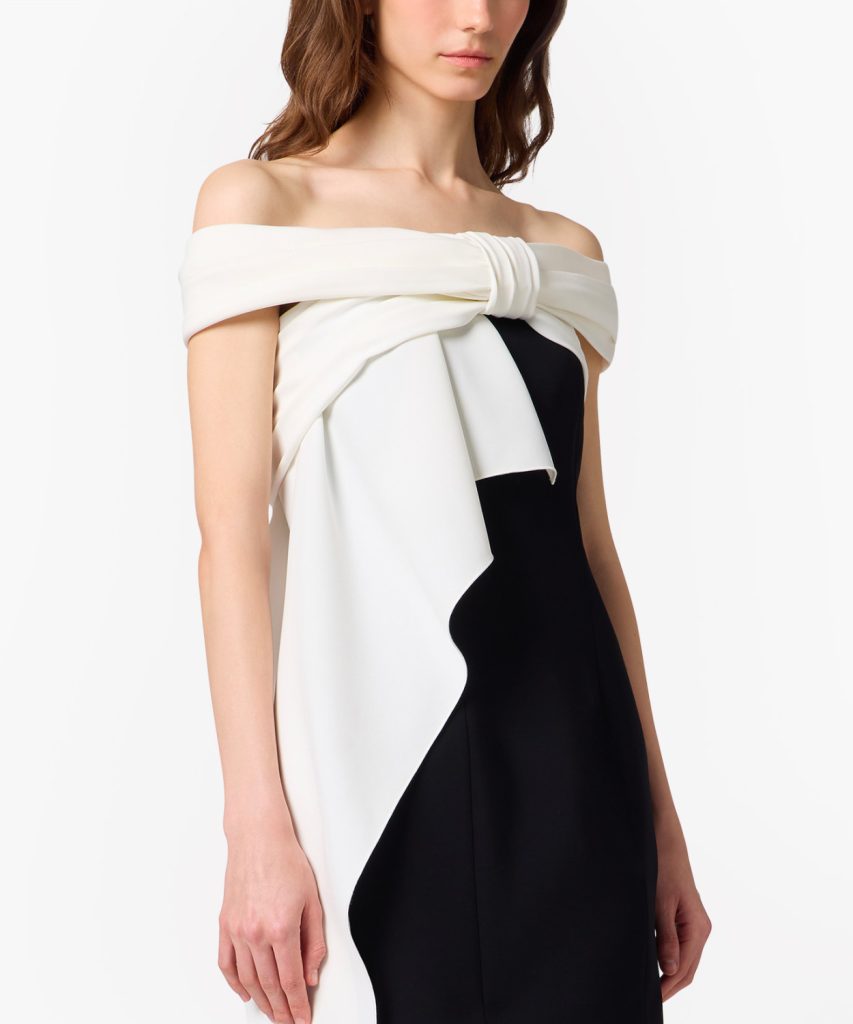 Off-shoulder black-and-white color-block dress with white draped fold across the chest and side knot detail on a model's torso.