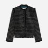 Black-and-white tweed cropped jacket with fringe edges and button front rhythmically lined with dark buttons in a check pattern.