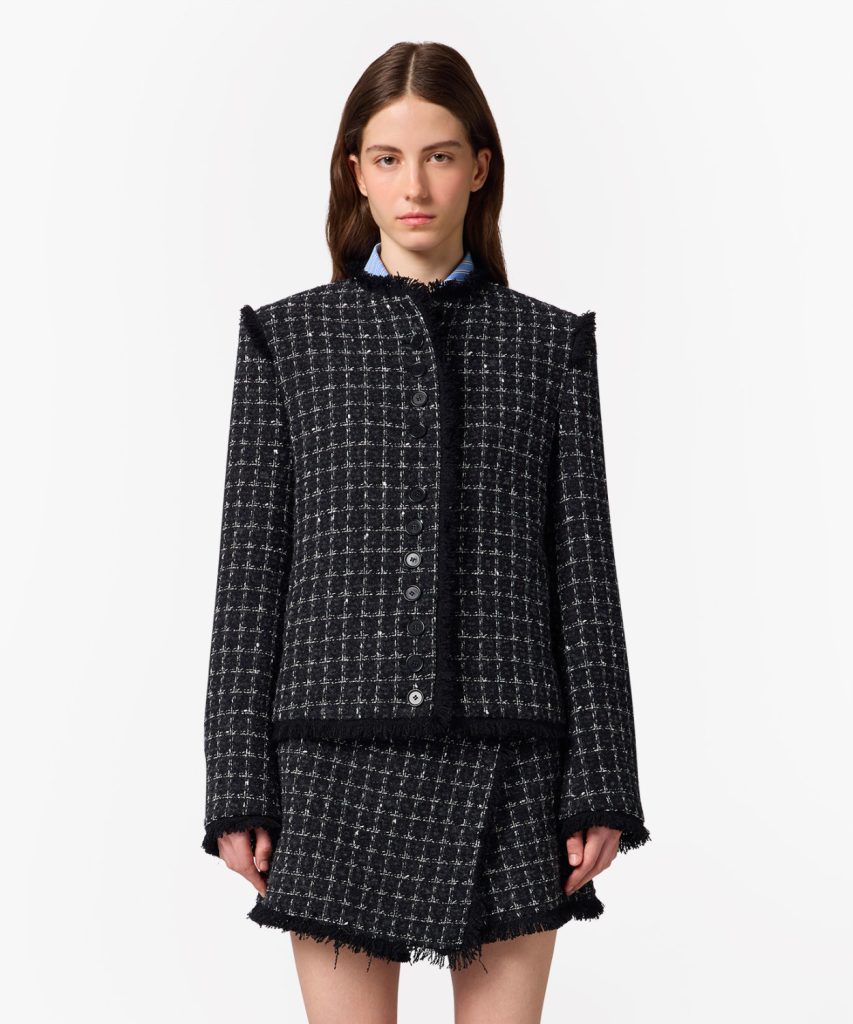 Model wearing a black-and-white checkered tweed jacket with fringe trim and a matching skirt/ensemble.